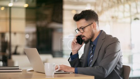 Téléchargez les photos : Homme d'affaires travaillant sur ordinateur et parlant sur son téléphone - en image libre de droit