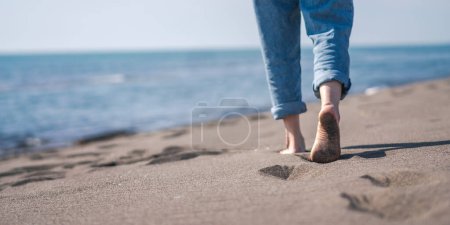 Téléchargez les photos : Femme marchant pieds nus sur la plage de sable fin. Pas de visage, jambes en jeans - en image libre de droit