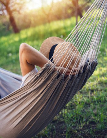 Téléchargez les photos : Femme dans un chapeau sur un hamac dans un jardin d'été. Vacances d'été - en image libre de droit