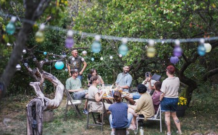 Foto de Picnic en el campo. Grupo de jóvenes amigos sentados en el jardín disfrutando de la cena juntos - Imagen libre de derechos