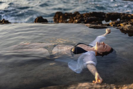 Téléchargez les photos : Jeune femme joyeuse et détendue dans un bain de mer naturel au bord de la mer. Concept de bien-être thalassothérapie - en image libre de droit