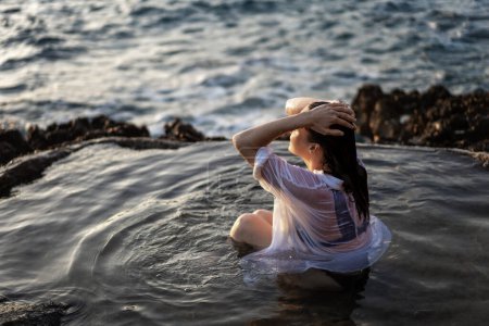 Téléchargez les photos : Jeune femme joyeuse et détendue en chemise blanche dans un bain de mer naturel au bord de la mer. Concept de bien-être thalassothérapie - en image libre de droit