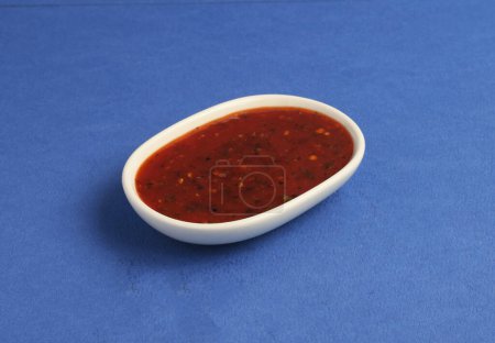 Ketchup en tazón aislado sobre fondo blanco y azul.