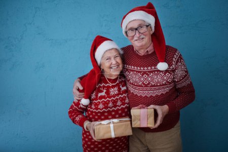 Foto de Retrato de feliz pareja de ancianos sosteniendo regalos, frente al fondo azul. - Imagen libre de derechos