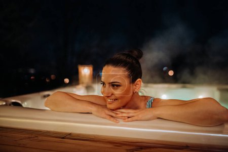 Photo for Young woman enjoying outdoor bathtub in her terrace during a cold winter evening. - Royalty Free Image