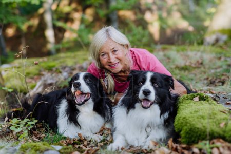 Retrato de mujer mayor con sus perros en un bosque.