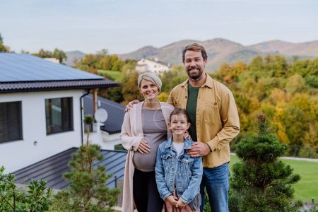 Téléchargez les photos : Famille heureuse près de leur maison avec des panneaux solaires. Énergie alternative, économies de ressources et concept de mode de vie durable. - en image libre de droit