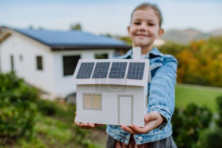 Primer plano de niña feliz sosteniendo el modelo de papel de la casa con los paneles solares.Energía alternativa, ahorro de recursos y concepto de estilo de vida sostenible.