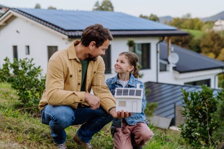 Little girl with her father holding paper model of house with the solar panels, explaining how it works.Alternative energy, saving resources and sustainable lifestyle concept.