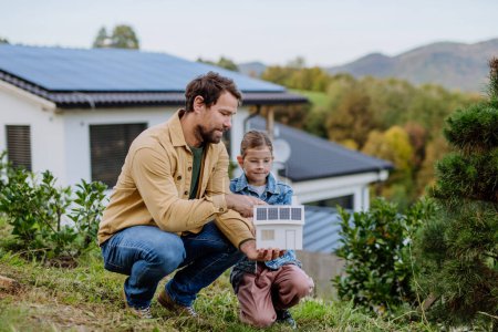 Téléchargez les photos : Petite fille avec son père tenant une maquette en papier de la maison avec les panneaux solaires, expliquant comment cela fonctionne.. - en image libre de droit