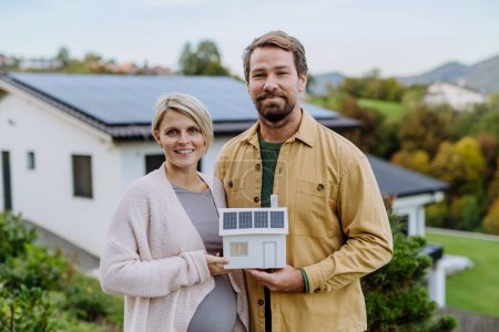 Téléchargez les photos : Gros plan d'un couple heureux tenant un modèle de papier de maison avec des panneaux solaires. Énergie alternative, économies de ressources et concept de mode de vie durable. - en image libre de droit