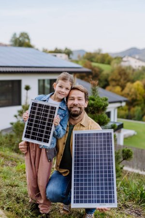 Père avec sa petite fille près de la maison avec des panneaux solaires. Énergie alternative, économies de ressources et concept de mode de vie durable.