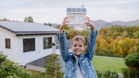 Photo for Happy girl holding paper model of house with the solar panels.Alternative energy, saving resources and sustainable lifestyle concept. - Royalty Free Image