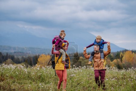 Glückliche Eltern mit ihren kleinen Kindern huckepack beim Herbstspaziergang inmitten der farbenfrohen Natur. Konzept eines gesunden Lebensstils.