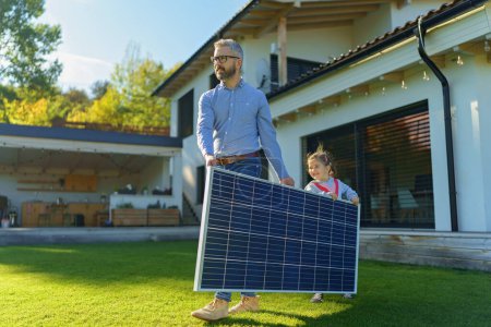 Père avec sa petite fille portant un panneau solaire dans la cour. Énergie alternative, économies de ressources et concept de mode de vie durable.