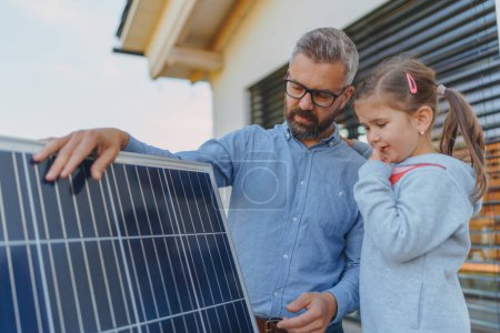 Foto de Padre mostrando a su pequeña hija paneles fotovoltaicos solares, explicando cómo funciona. Energía alternativa, ahorro de recursos y concepto de estilo de vida sostenible. - Imagen libre de derechos