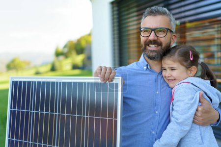Téléchargez les photos : Père avec sa petite fille près de la maison avec des panneaux solaires. Énergie alternative, économies de ressources et concept de mode de vie durable. - en image libre de droit