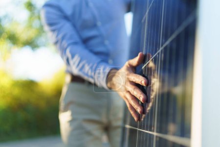 Close-up of businessman holding solar panel, standing outdoor at a garden.