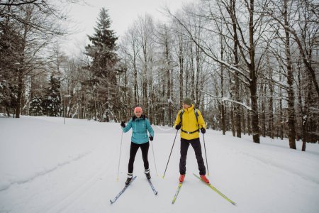 Couple de personnes âgées skient ensemble au milieu de la forêt enneigée