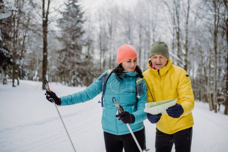 Téléchargez les photos : Couple âgé regardant la carte sur papier pendant le ski de fond dans la nature enneigée. - en image libre de droit