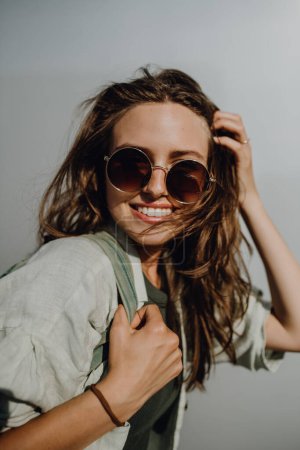 Porträt einer glücklichen jungen Frau im Freien mit Rucksack und Sonnenbrille.