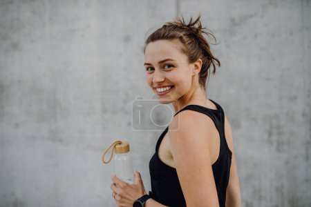 Téléchargez les photos : Jeune femme boire de l'eau pendant le jogging dans une ville, mode de vie sain et concept sportif. - en image libre de droit