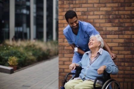Téléchargez les photos : Heureuse femme âgée dans un fauteuil roulant passant du temps dehors avec son assistante. - en image libre de droit