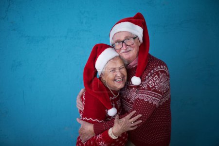 Photo for Portrait of happy senior couple in Christmas sweaters hugging,in front of blue background. - Royalty Free Image