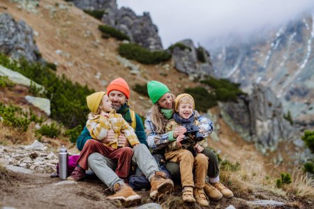 Foto de Feliz familia sentada y descansando, durante el senderismo juntos en una montaña de otoño. - Imagen libre de derechos