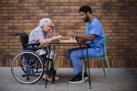 Pfleger spielt Schach mit seinem Klienten im Freien in einem Café.