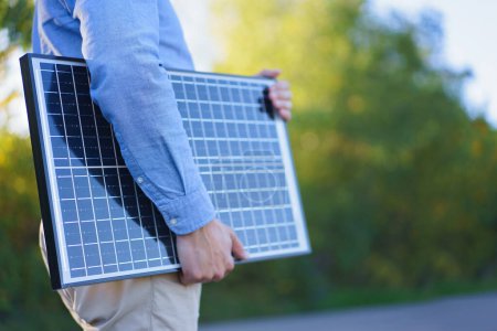 Téléchargez les photos : Partie médiane d'un homme d'affaires tenant un panneau solaire, debout à l'extérieur dans un jardin. - en image libre de droit