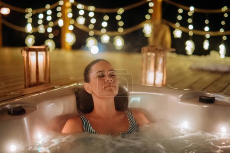 Photo for Young woman enjoying outdoor bathtub in her terrace during a cold winter evening. - Royalty Free Image