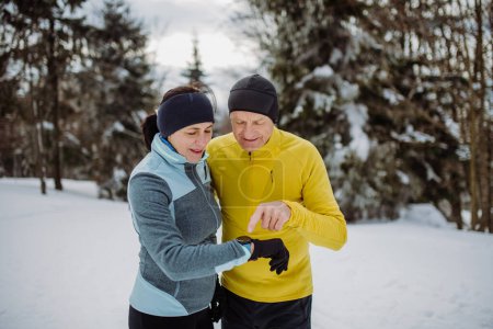 Photo for Senior couple looking at a smartwatch during winter run. - Royalty Free Image