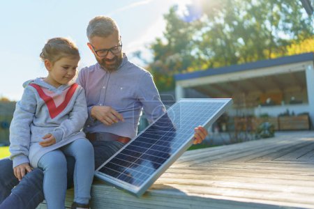 Téléchargez les photos : Père montrant à sa petite fille un panneau solaire photovoltaïque, expliquant comment ça marche. Énergie alternative, économies de ressources et concept de mode de vie durable. - en image libre de droit