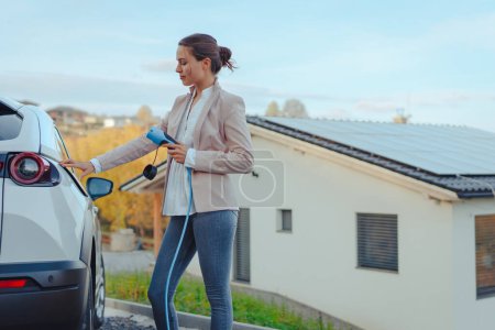 Young woman charging electric car in home, sustainable and economic transportation concept.