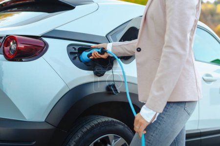 Primer plano de la mujer sosteniendo el cable de alimentación de su coche, cargándolo en el hogar, concepto de transporte sostenible y económico.
