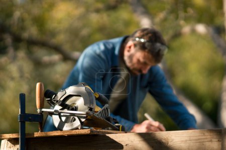 Photo for Mature handyman measuring a board, outside in garden. - Royalty Free Image