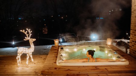 Young woman enjoying outdoor bathtub in her terrace during a cold winter evening.