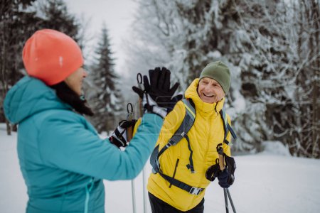 Photo for Senior couple skiing together in the middle of snowy forest, having break and giving high five. - Royalty Free Image