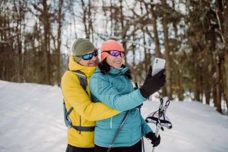 Téléchargez les photos : Couple de personnes âgées prenant selfie pendant le ski de fond dans la nature enneigée. - en image libre de droit