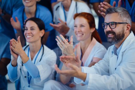 Photo for Portrait of happy doctors, nurses and other medical staff clapping, in a hospital. - Royalty Free Image