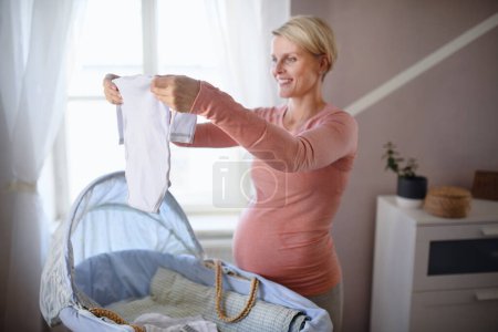 Foto de Mujer embarazada feliz mirando poca ropa de bebé. - Imagen libre de derechos