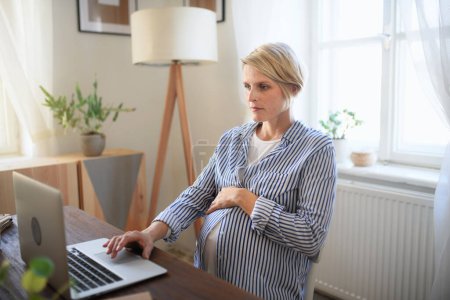 Téléchargez les photos : Heureuse femme enceinte ayant son bureau dans un salon. - en image libre de droit