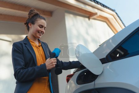 Mujer joven sosteniendo cable de alimentación de su coche, preparada para cargarlo en el hogar, concepto de transporte sostenible y económico.