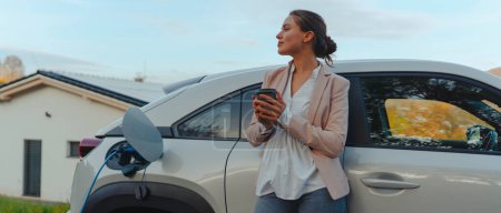Mujer joven con taza de café esperando mientras se carga el coche eléctrico, concepto de transporte sostenible y económico.