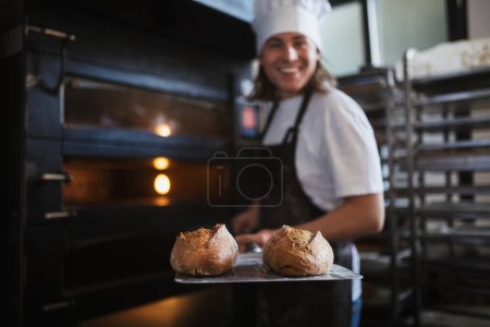Happy young baker with fresh bread, in a bakery.