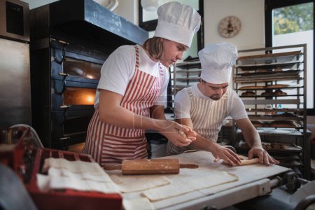 Téléchargez les photos : L'homme au syndrome du duvet aide à préparer le pain dans une boulangerie avec son collègue. Concept d'intégration des personnes handicapées dans la société. - en image libre de droit