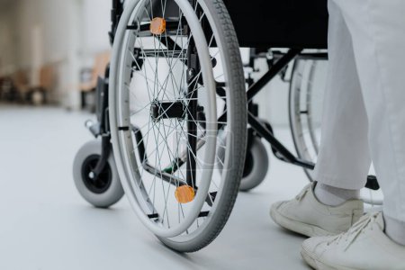 Photo for Rear view of caregiver pushing wheelchiar at a corridor in hospital. - Royalty Free Image