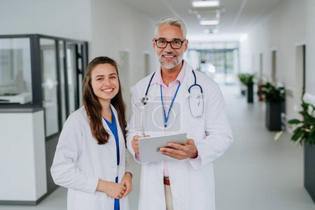 Photo for Portrait of elderly doctor with his younger colleague at a hospital corridor. Health care concept. - Royalty Free Image