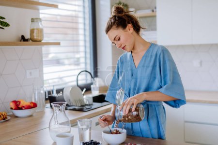 Foto de Mujer joven preparando un muesli para el desayuno en su cocina, rutina de la mañana y el concepto de estilo de vida saludable. - Imagen libre de derechos